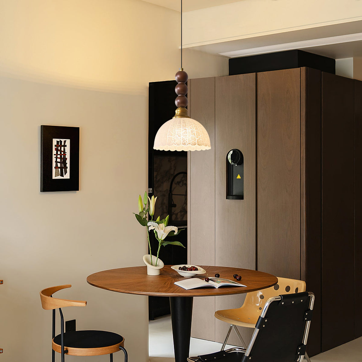 Wider view of a Clérachic pendant with a small scalloped shade above a round walnut table and black-and-tan chairs.