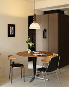 A Clérachic pendant hangs in a warm-toned dining nook, with a round table, flowers and two chairs below it.