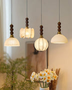 The four Clérachic pendants shown in a vertical frame, shades glowing against a soft beige wall with daffodils below.