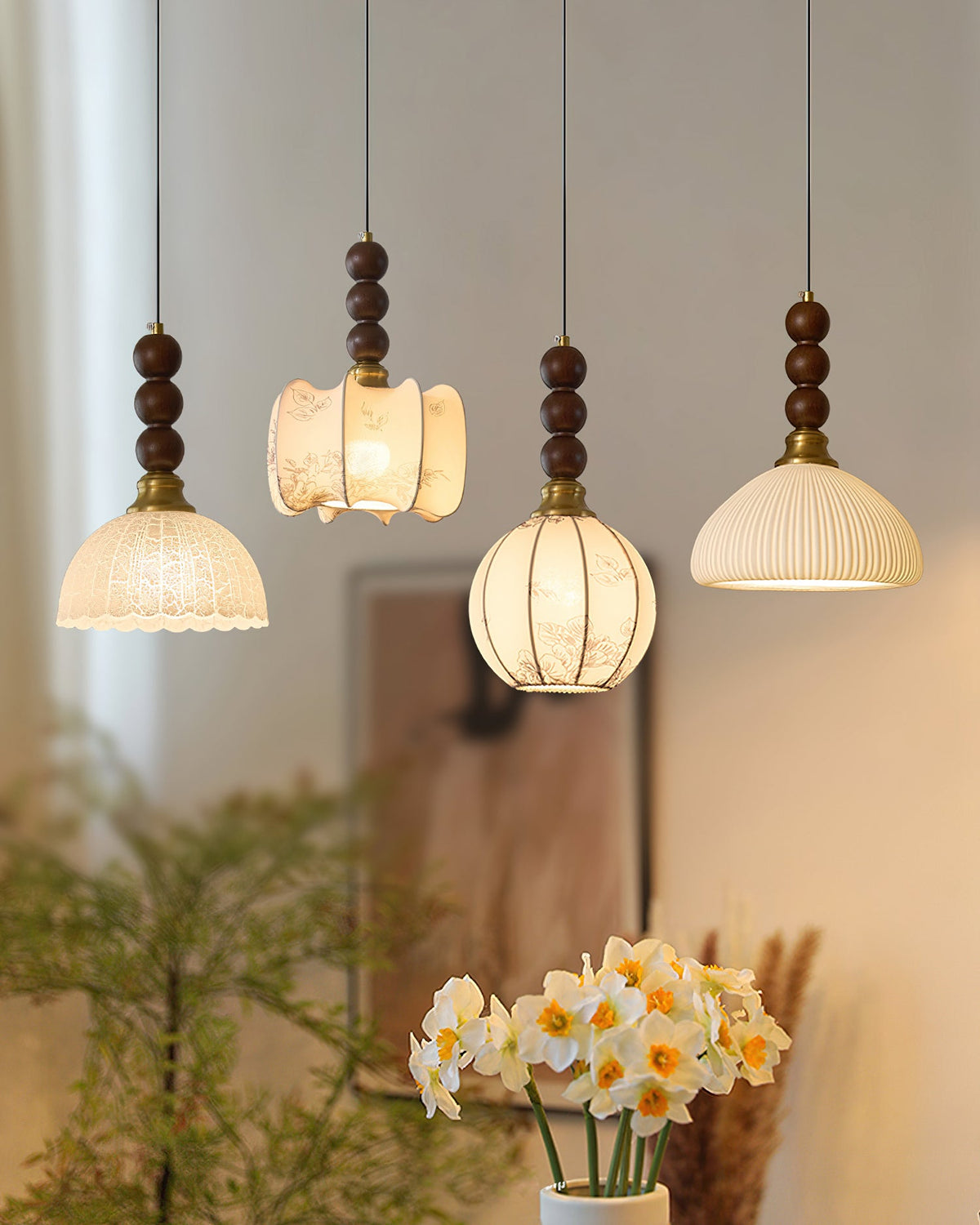 The four Clérachic pendants shown in a vertical frame, shades glowing against a soft beige wall with daffodils below.