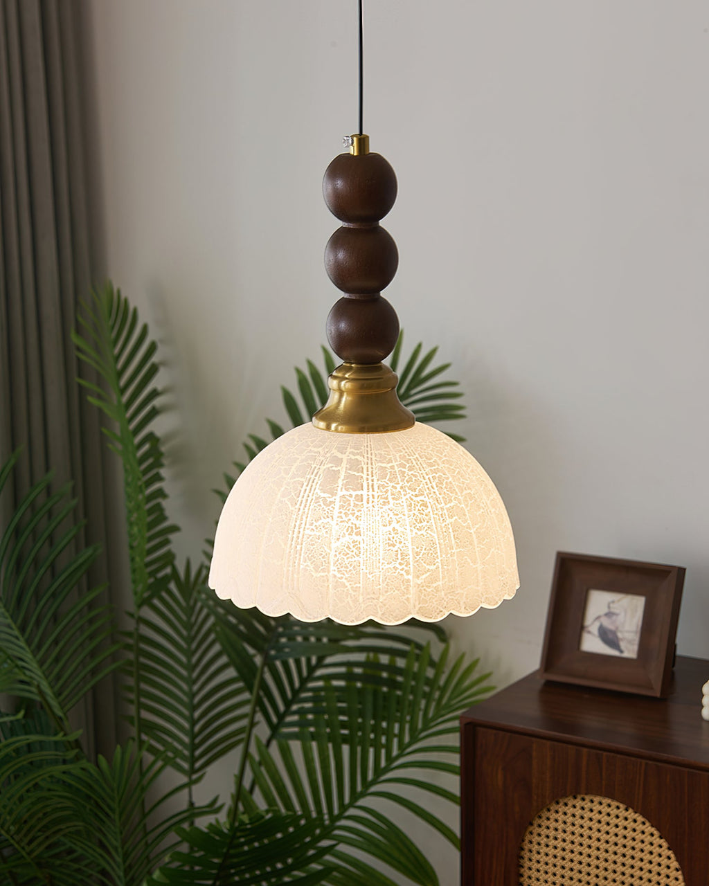 Frosted dome shade with a scalloped edge on this Clérachic pendant, with a houseplant and a small framed picture behind.