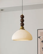 Another angle of the ribbed ceramic Clérachic pendant, with its brass collar and walnut beads below a white ceiling.