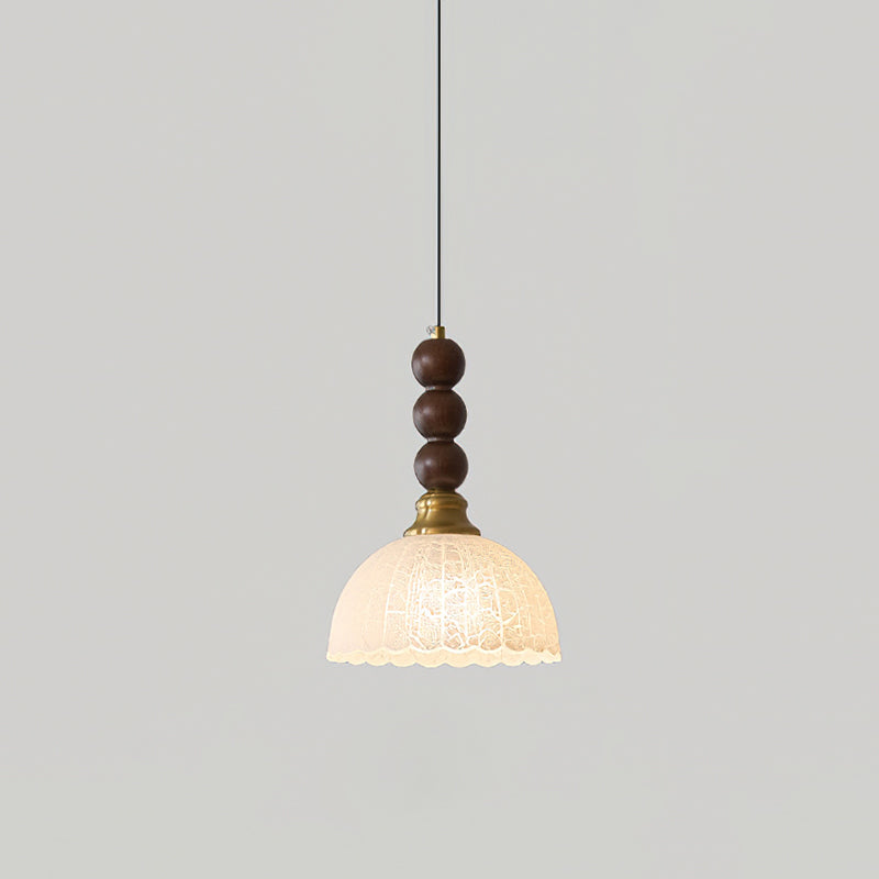 A Clérachic pendant with a small frosted scalloped shade and walnut beads hangs against a plain light grey wall.