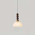 A Clérachic pendant with a small frosted scalloped shade and walnut beads hangs against a plain light grey wall.