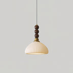A ribbed ceramic Clérachic pendant with a brass collar and walnut beads, hung against a plain light grey wall.