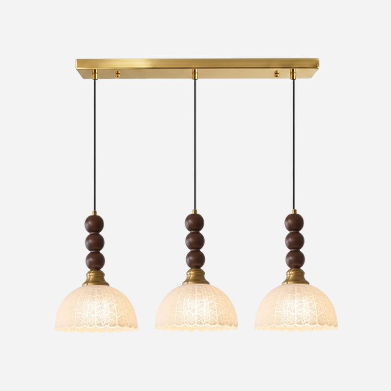 Three frosted-shade Clérachic pendants hang from one long brass bar canopy, each with stacked walnut beads.