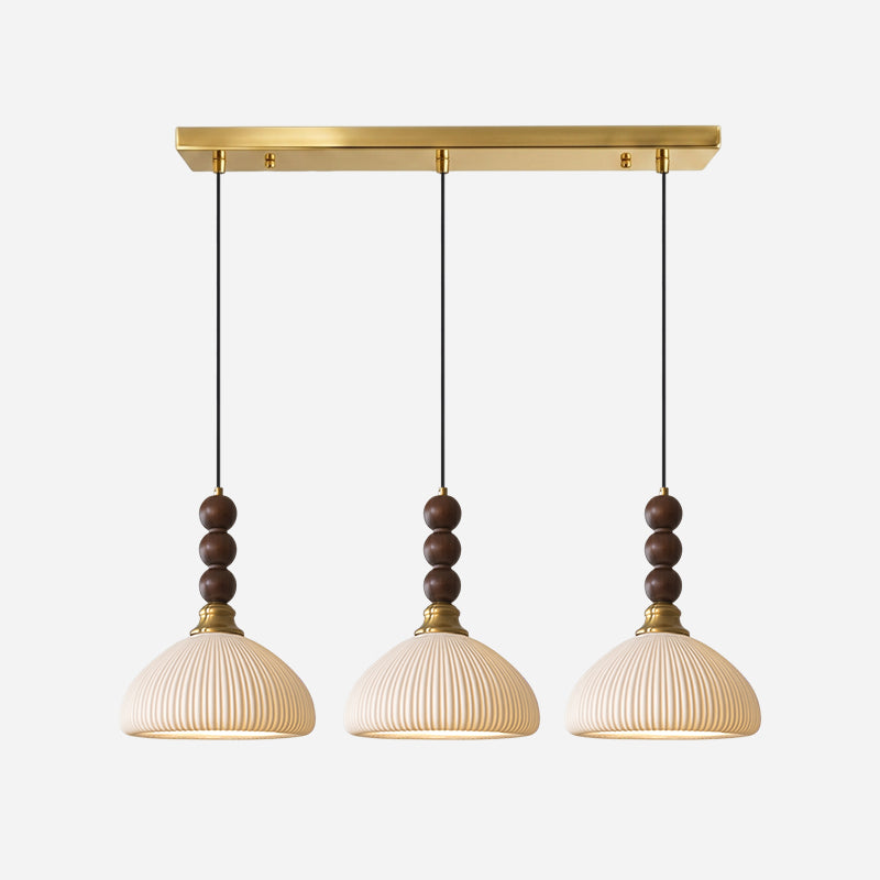 Three ribbed ceramic Clérachic pendants hang from a long brass bar canopy, shown on a pale grey backdrop.