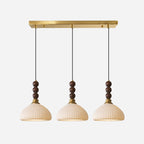 Three ribbed ceramic Clérachic pendants hang from a long brass bar canopy, shown on a pale grey backdrop.