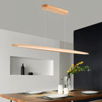 A Clérachic beech pendant glows along its underside above a live-edge dining table set with plates, in a grey room with a niche.