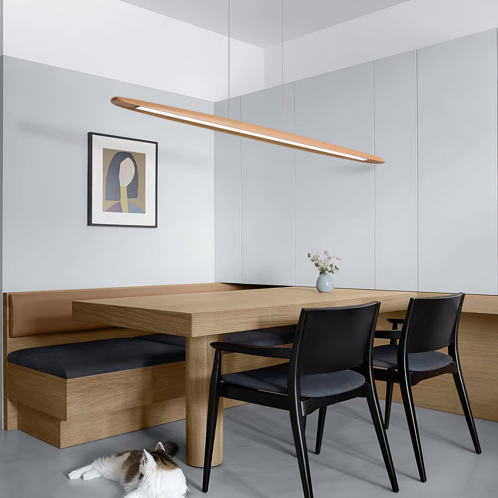 A Clérachic beech pendant hangs at a tilt above a pale wood dining nook with black chairs and a cat on the floor.