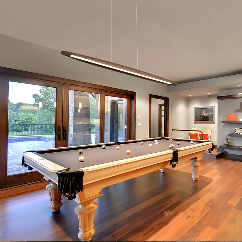 A Clérachic wood pendant hangs over a billiards table in a room with wooden floors and tall glass doors.