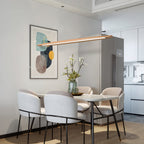 A Clérachic beech pendant tilts above a white dining table with pale curved chairs, beside an abstract print.
