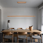 A Clérachic beech pendant hangs from its wooden canopy above a long timber table in a pale grey dining room.