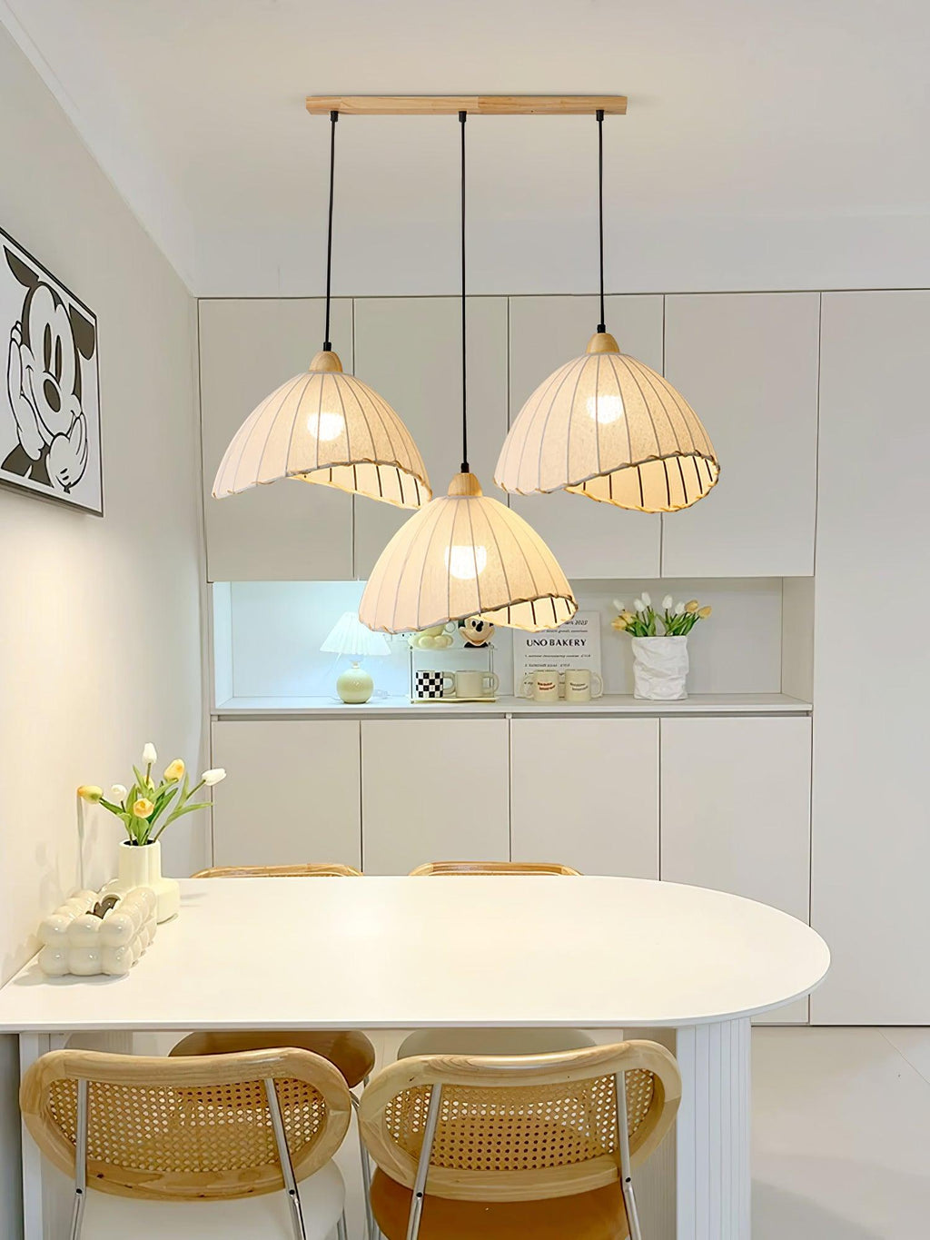 Clérachic swept-hem pendant lamp as a three-light fitting over a white oval dining table, the fitted kitchen units behind it.