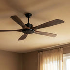Angled view of the Clérachic fan with dark wood blades and a black motor and light disc, near a window with linen curtains.