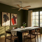 Clérachic ceiling fan with light wood blades and a white motor above a dark dining table in a green-walled room with large windows.