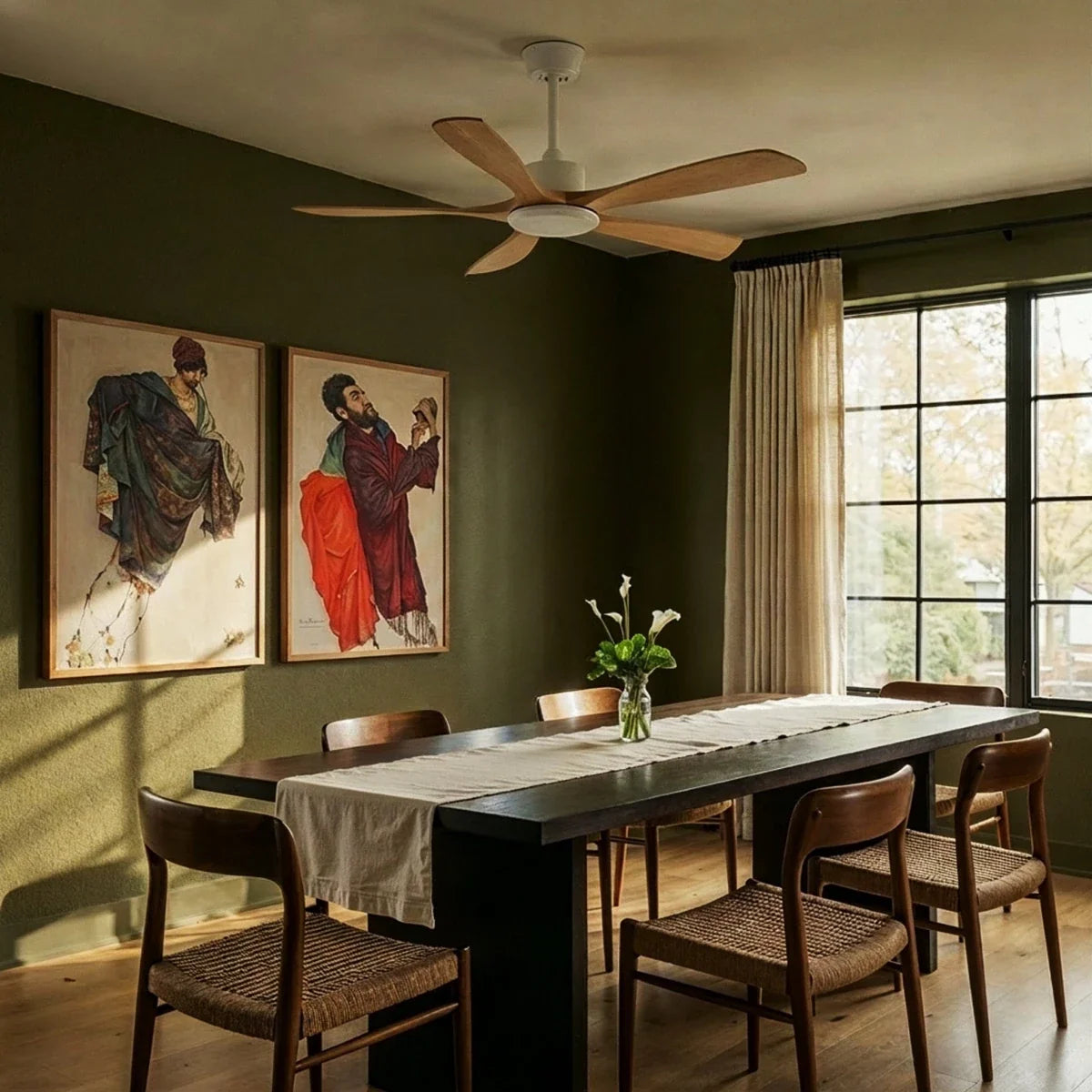 Clérachic ceiling fan with light wood blades and a white motor above a dark dining table in a green-walled room with large windows.