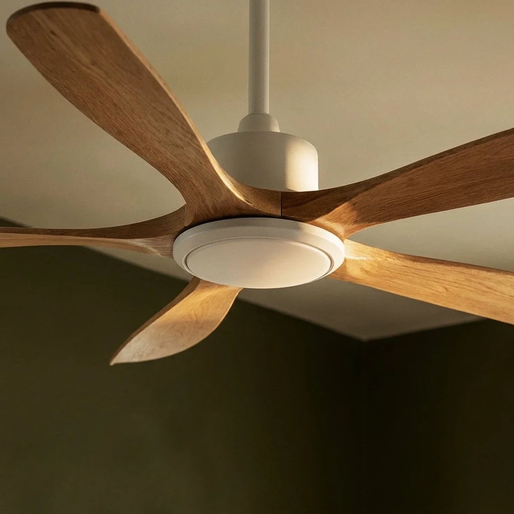 Clérachic ceiling fan in white and pale wood seen from below, showing its round light disc and curved blades in soft side light.