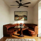 Clérachic ceiling fan with dark wood blades and a black motor above a curved banquette and pedestal table in a bright alcove.
