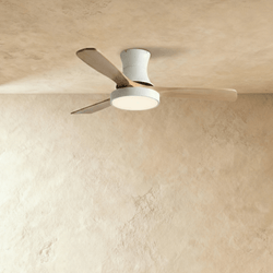 Clérachic low-profile ceiling fan in white with three pale wood blades and its round LED light switched on, against limewash.