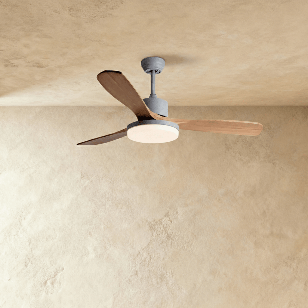 Clérachic ceiling fan on a grey downrod with three warm wood blades and a round LED light glowing below the motor.