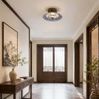 A Clérachic ceiling light hangs in a calm entry hall with a dark console table, a tall vase and a framed landscape print.