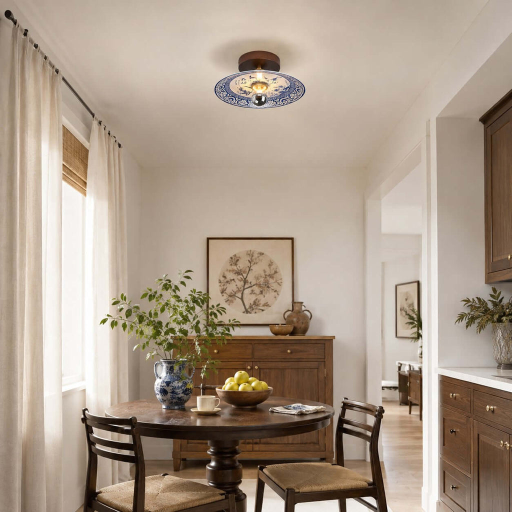 A Clérachic ceiling light above a small round dining table with a bowl of lemons, beside a window with sheer curtains.