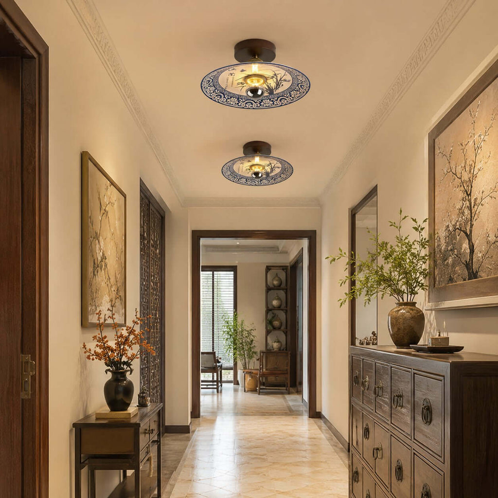 Two Clérachic ceiling lights in a row along a hallway, above a carved chest of drawers and framed branch prints.