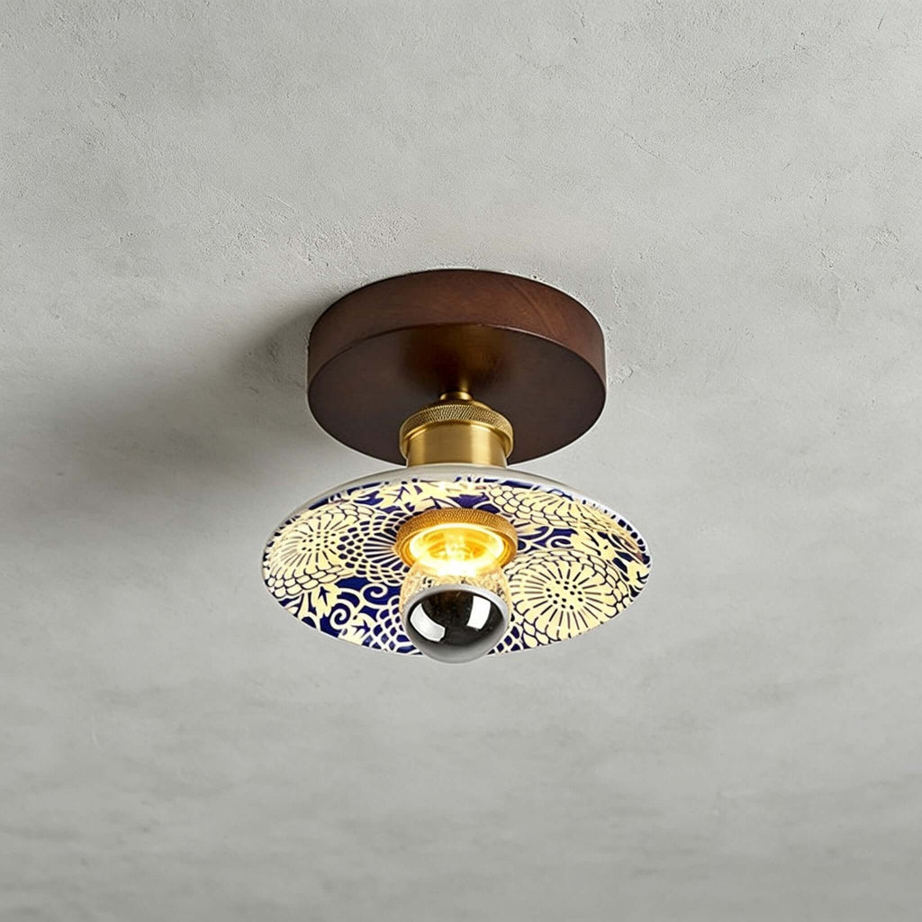 A Clérachic ceiling light with a cream shade patterned in blue and yellow, a round wood canopy and a brass fitting above.