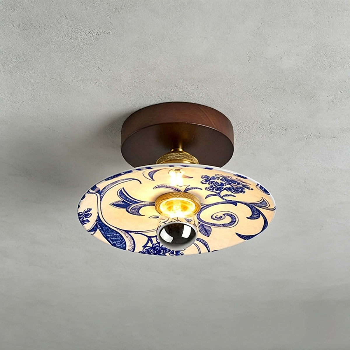 This Clérachic ceiling light has a wide shade painted with blue scrolls and flowers, under a round wood canopy.
