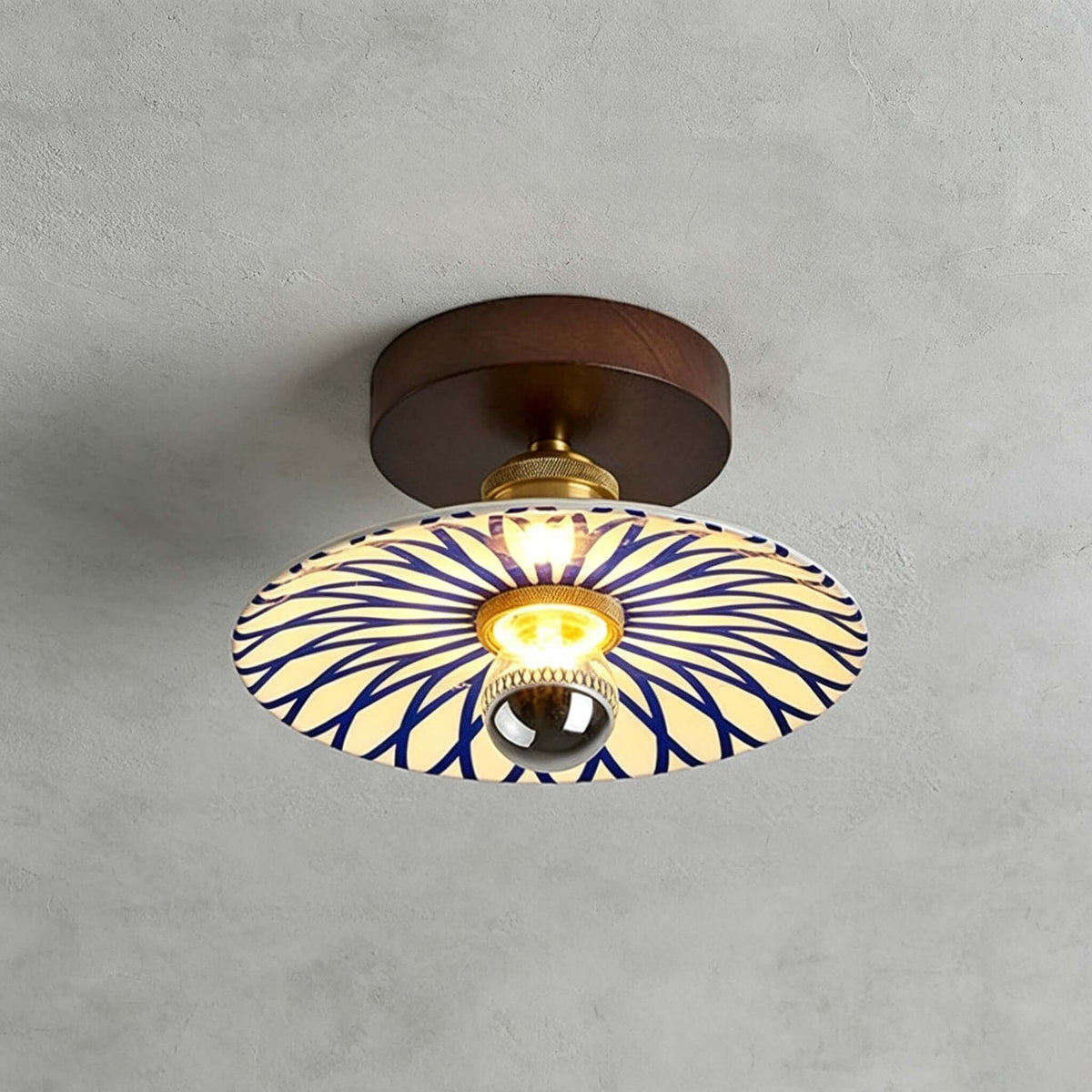 A Clérachic ceiling light with a sunburst of blue lines across its cream shade, fixed to the ceiling by a round wood canopy.