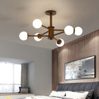 Walnut-toned Clérachic ceiling light with six white globes, lit over a bedroom with a grey tufted headboard and wood wall panelling.