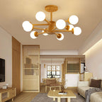 Lit globes on the pale wooden arms of this Clérachic ceiling light, in a living room with a low wooden coffee table and slatted screen.
