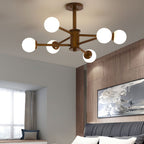 Close view of a walnut-toned Clérachic ceiling light with six white globes, with a bedroom and a framed abstract print below.