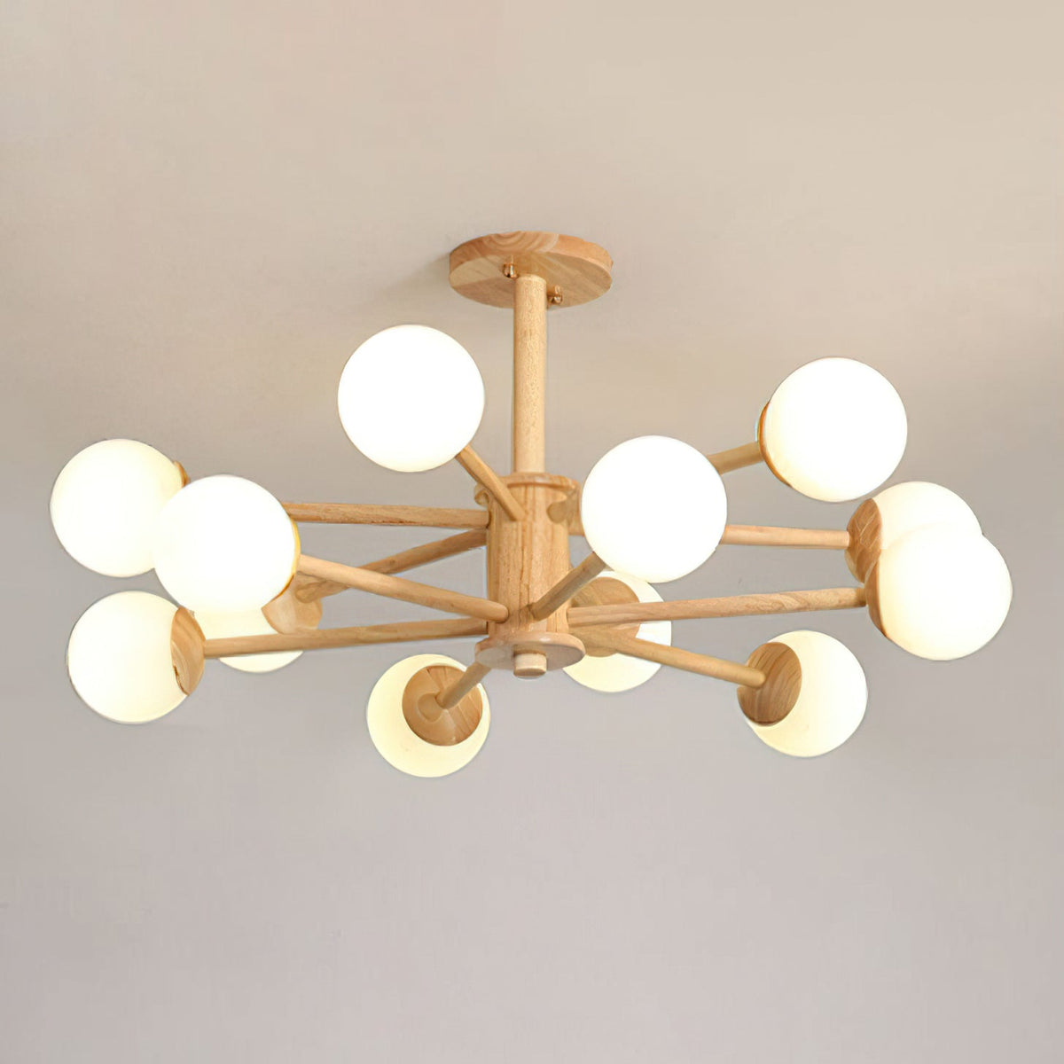 Light wood arms carry a dozen white globes on this Clérachic ceiling light, shown against a soft grey ceiling.