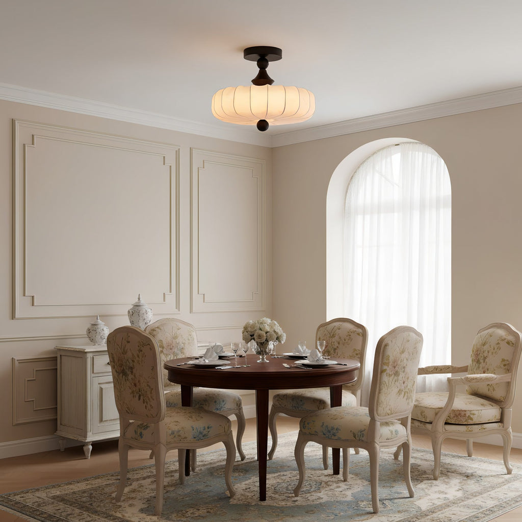 This Clérachic ceiling light glows above a round dining table with floral-upholstered chairs, in a panelled room with an arched window.