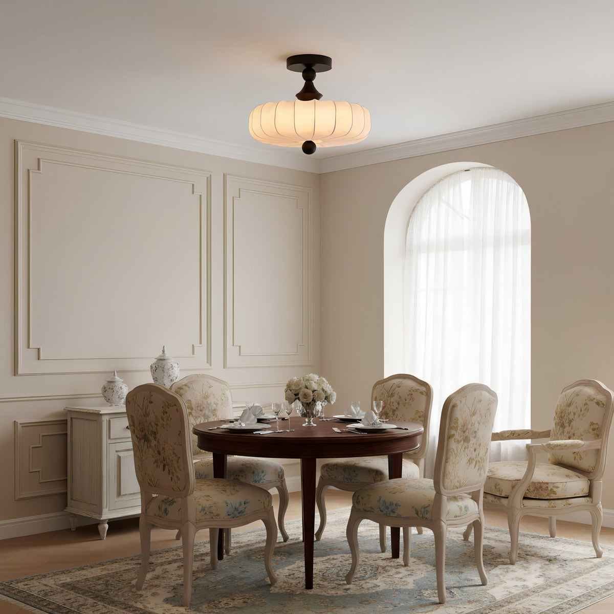 This Clérachic ceiling light glows above a round dining table with floral-upholstered chairs, in a panelled room with an arched window.