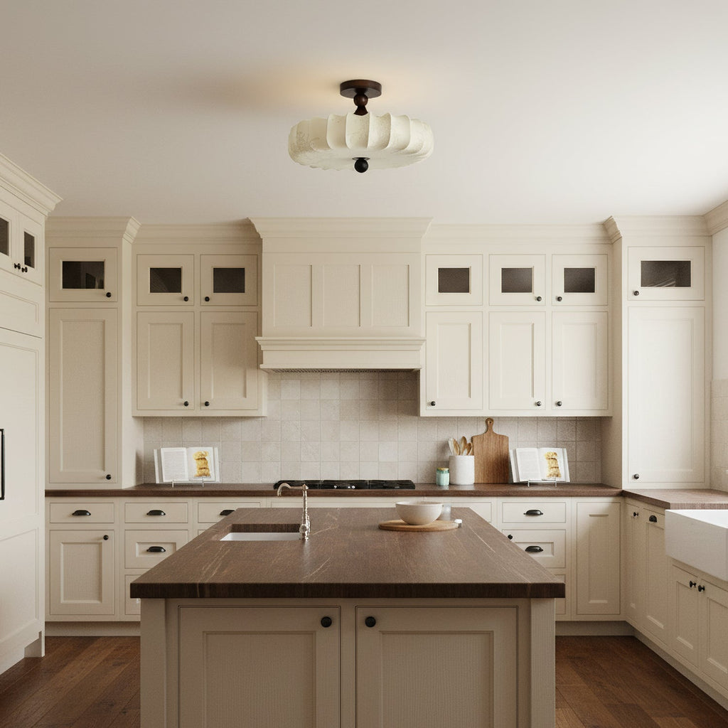 A Clérachic ceiling light with a pale pleated shade sits above a cream kitchen with a wooden island and a dark worktop.