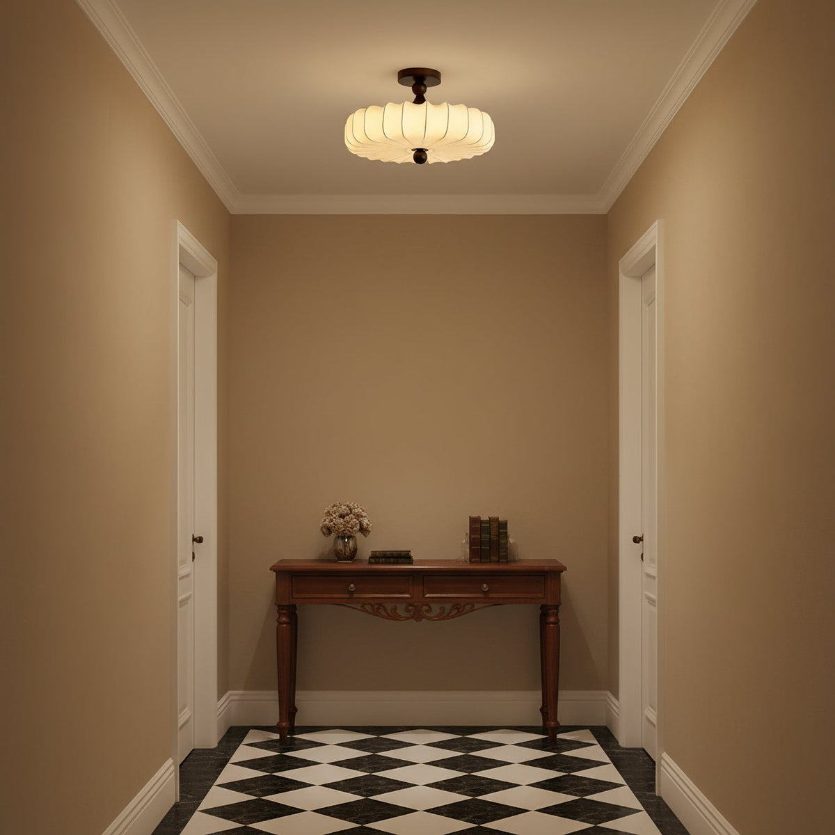A glowing Clérachic ceiling light with a pleated shade lights a small tan-walled hallway with a carved console table and a chequered floor.
