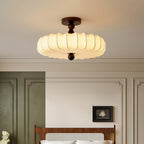 Close to the ceiling, a lit Clérachic light with a warm, softly pleated shade glows above a panelled wall and a rattan bedhead.
