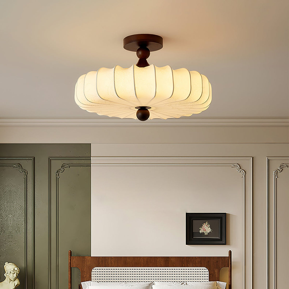 Close to the ceiling, a lit Clérachic light with a warm, softly pleated shade glows above a panelled wall and a rattan bedhead.