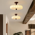 Two Clérachic ceiling lights, one above the other in perspective, glow beside a heavy timber beam in a hallway with a woven screen.
