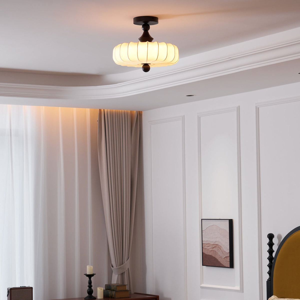 A lit Clérachic ceiling light with a smooth pleated shade hangs in a bedroom with a layered ceiling, long curtains and white wall panels.