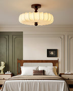 A wide Clérachic ceiling light with a warm pleated shade hangs above a panelled bedroom with a rattan headboard and olive-green wall.