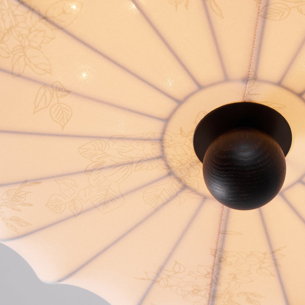 Looking up at the underside of this Clérachic ceiling light, the ribs of the fabric shade run out from a dark wooden finial, with faint leaf prints.