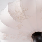 Close view of the fine printed leaf and flower pattern on the soft beige fabric of this Clérachic ceiling light, beside its round finial.