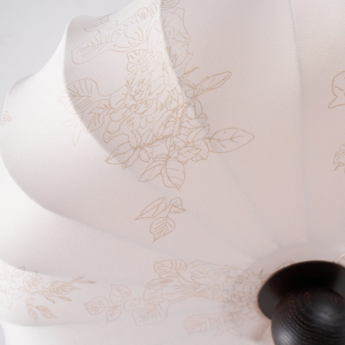 Close view of the fine printed leaf and flower pattern on the soft beige fabric of this Clérachic ceiling light, beside its round finial.