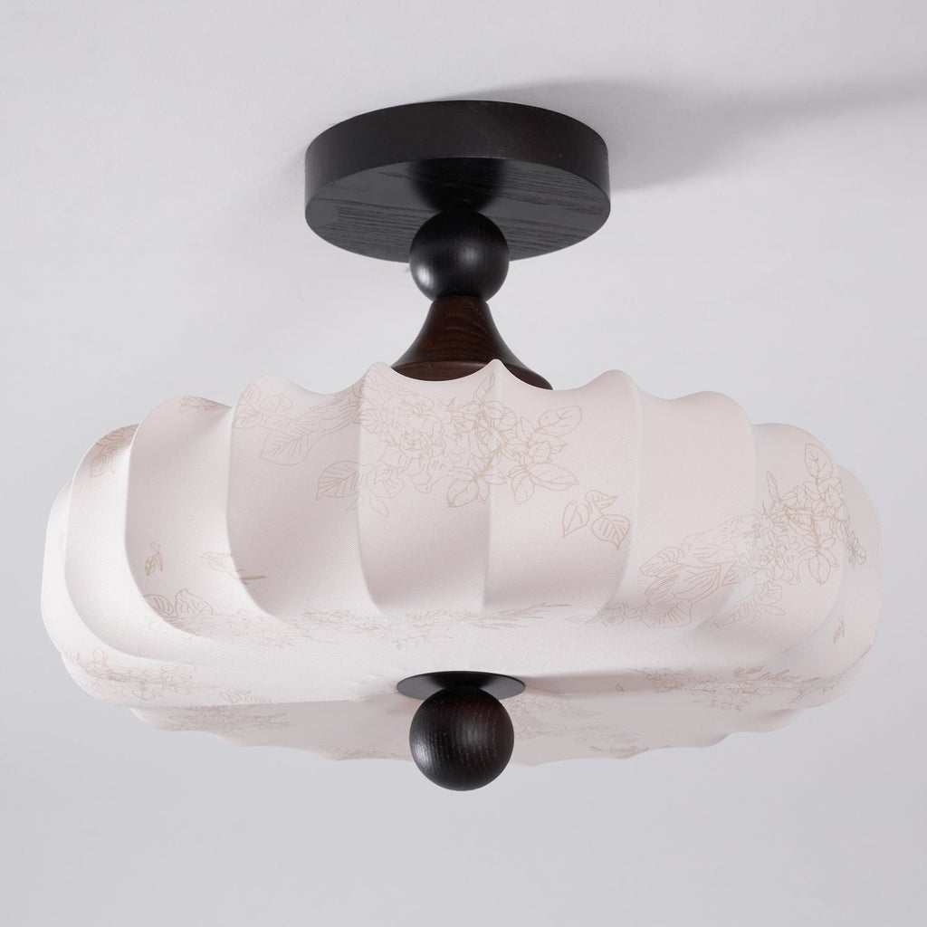 Seen from below at an angle, this Clérachic ceiling light shows its faint printed floral pattern and scalloped lower edge on the beige shade.