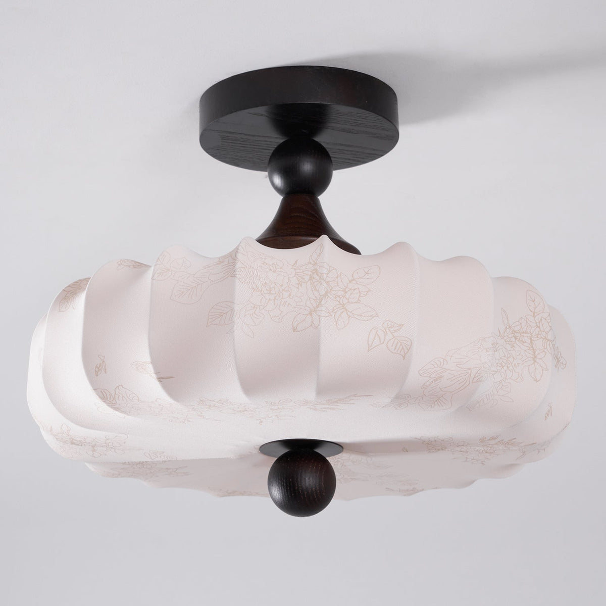 Seen from below at an angle, this Clérachic ceiling light shows its faint printed floral pattern and scalloped lower edge on the beige shade.
