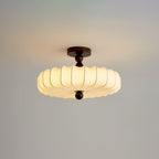A lit Clérachic ceiling light with a pleated cream shade and a dark canopy hangs against a soft grey-peach backdrop.